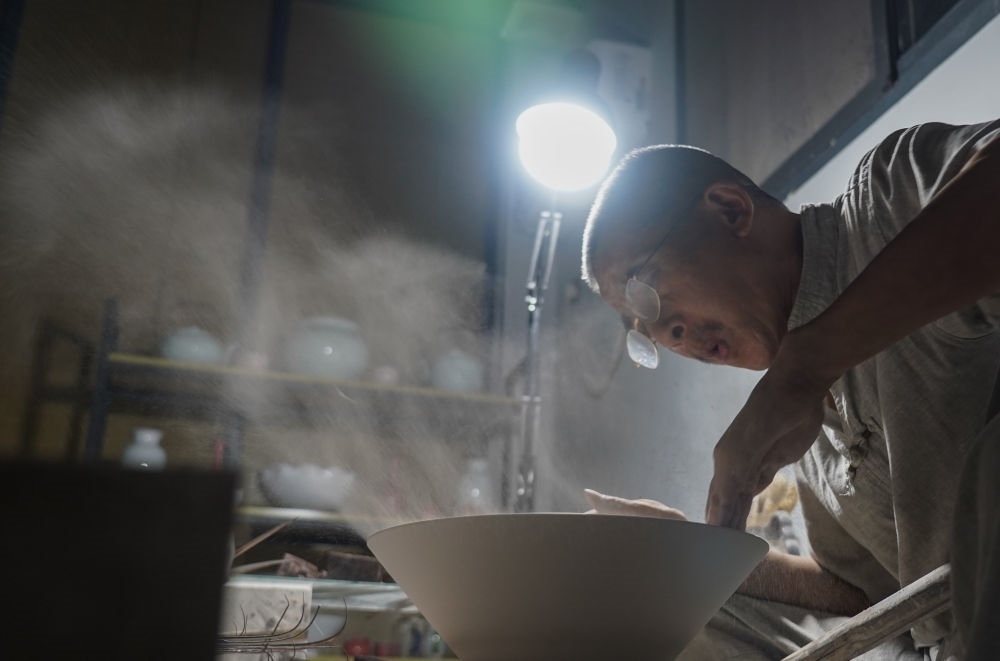 ↑ 在景德鎮(zhèn)，手工匠人吹去坯內(nèi)的泥土（2021年7月14日攝）。