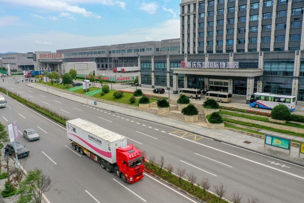 2023年10月11日，滿載筆記本電腦配件、發(fā)電機組件等產(chǎn)品的西部陸海新通道跨境公路班車從重慶南彭公路保稅物流中心駛出，將途經(jīng)廣西憑祥，直達越南（無人機照片）。新華社記者 黃偉 攝