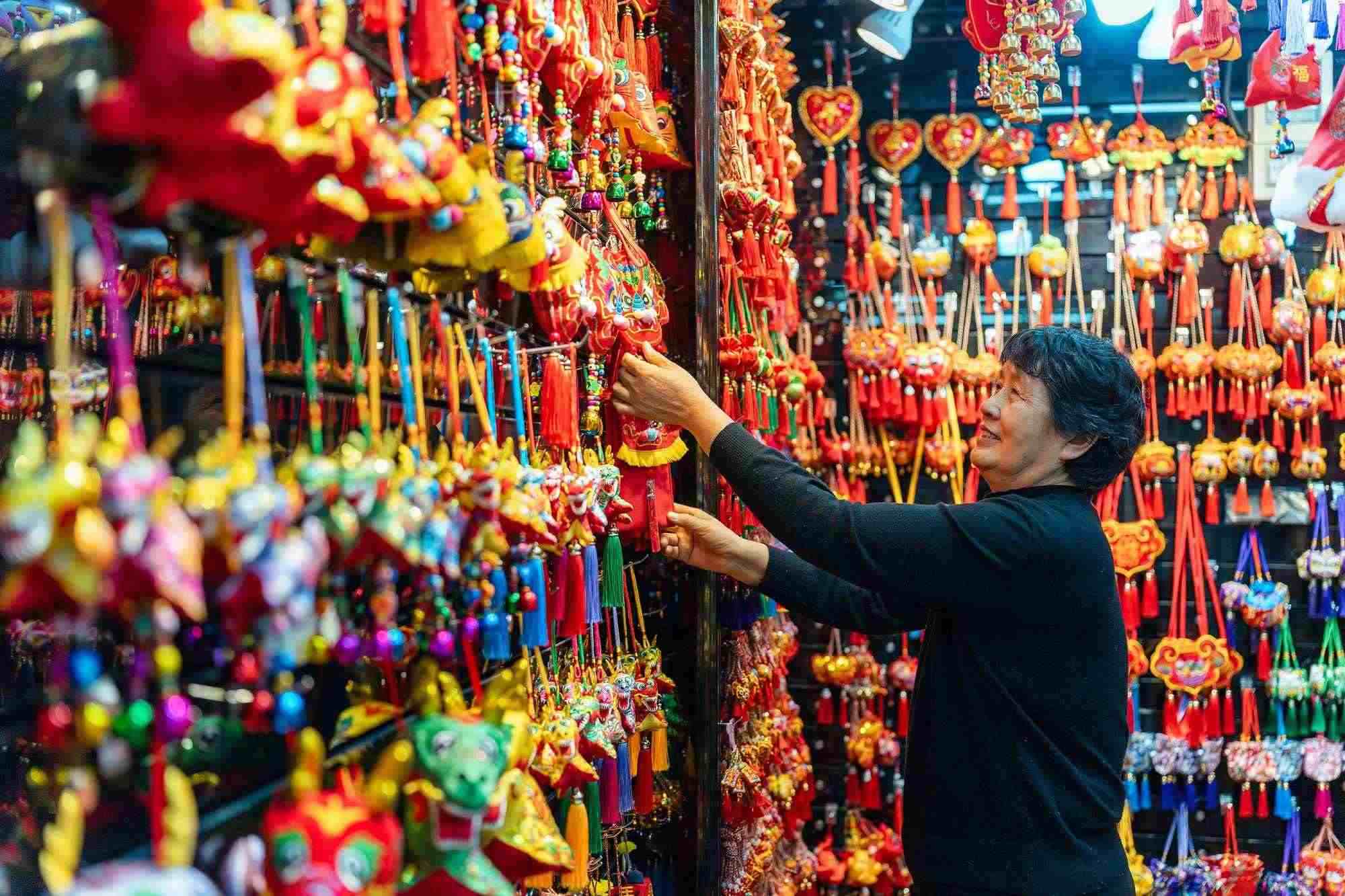 2023年12月11日，金華義烏國(guó)際商貿(mào)城，龍年喜慶用品掛滿攤位，顧客正在挑選中。