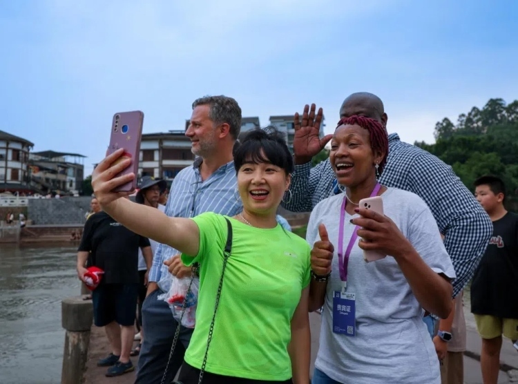 2024“一帶一路”媒體合作論壇聯(lián)合采訪調(diào)研行成員在樂山蘇稽古鎮(zhèn)與游客合影留念。本報記者 伊霄攝