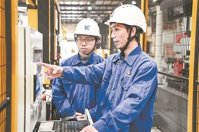 在廣西柳工機械股份有限公司生產(chǎn)車間內(nèi)，一名高級技師（右）給徒弟講解數(shù)控設(shè)備操作細節(jié)。新華社記者 曹祎銘攝